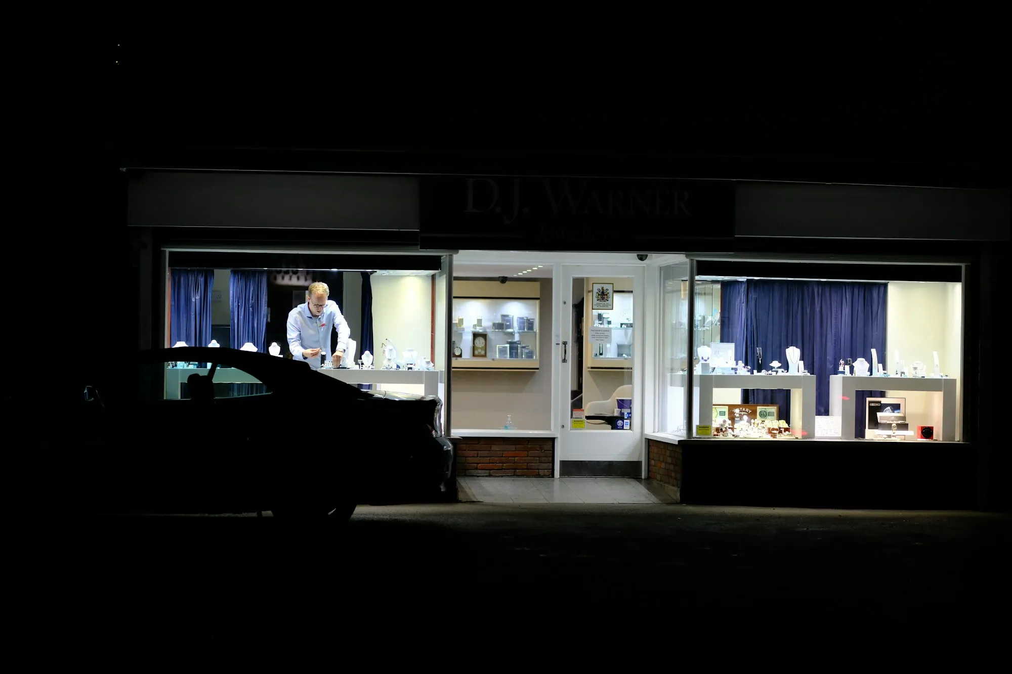 Vitrine de joalheria acesa numa rua escura, à noite